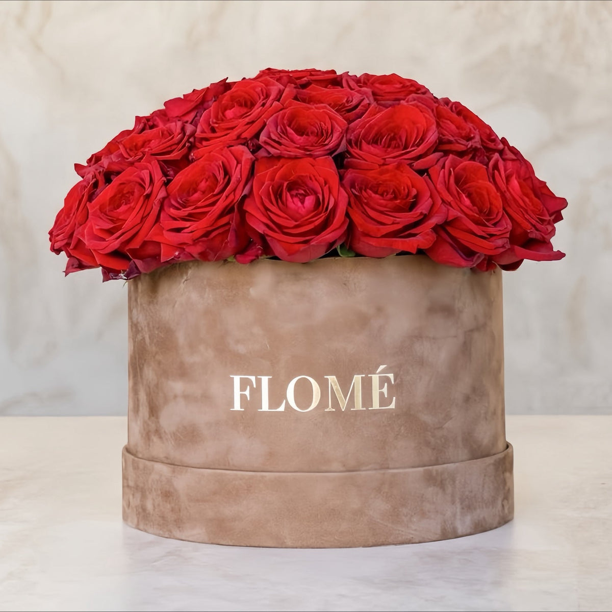 Dybrøde roser sat tæt i beige velouræske med Flomé-logo